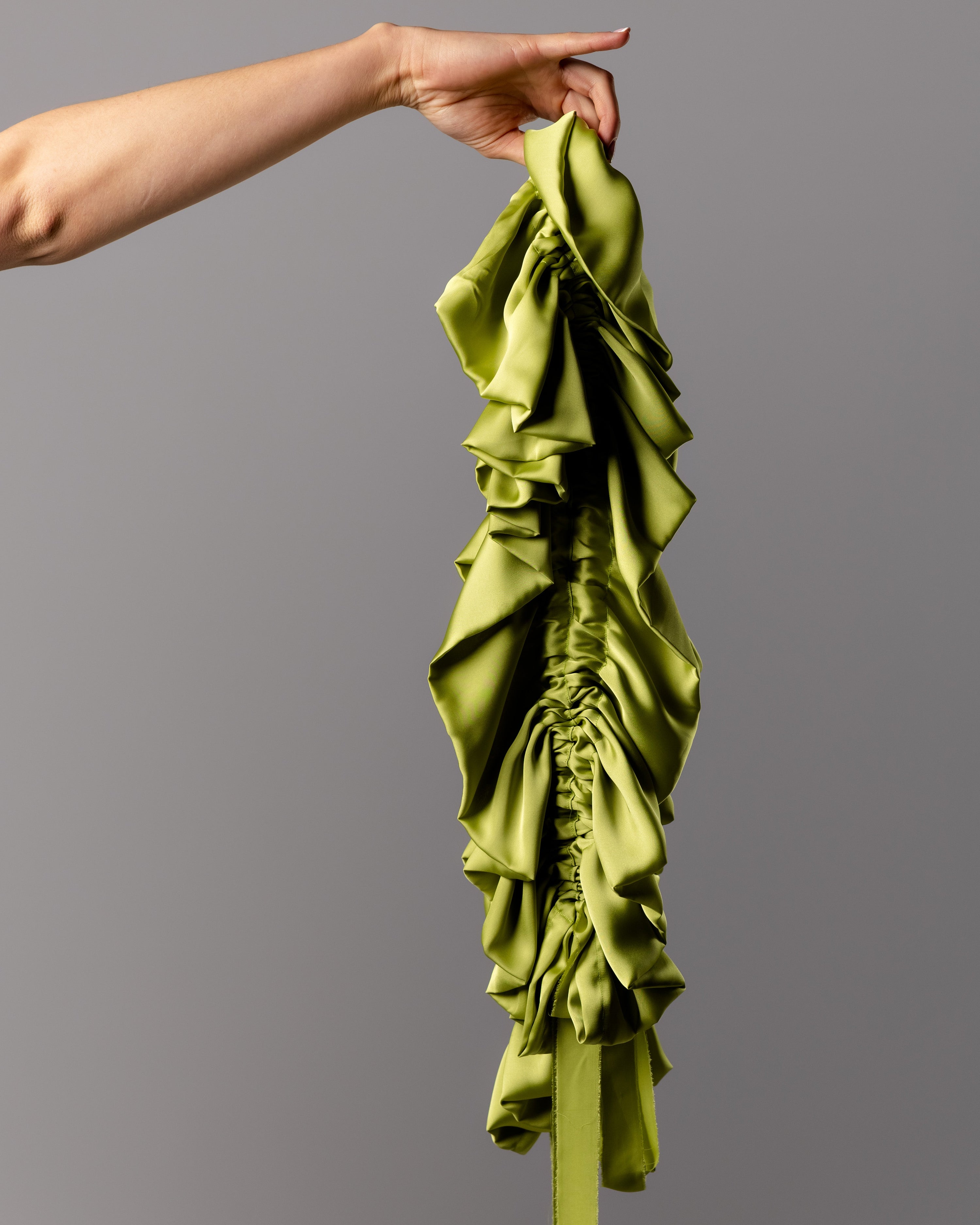 Green ruffled parasol held by a hand against a gray background